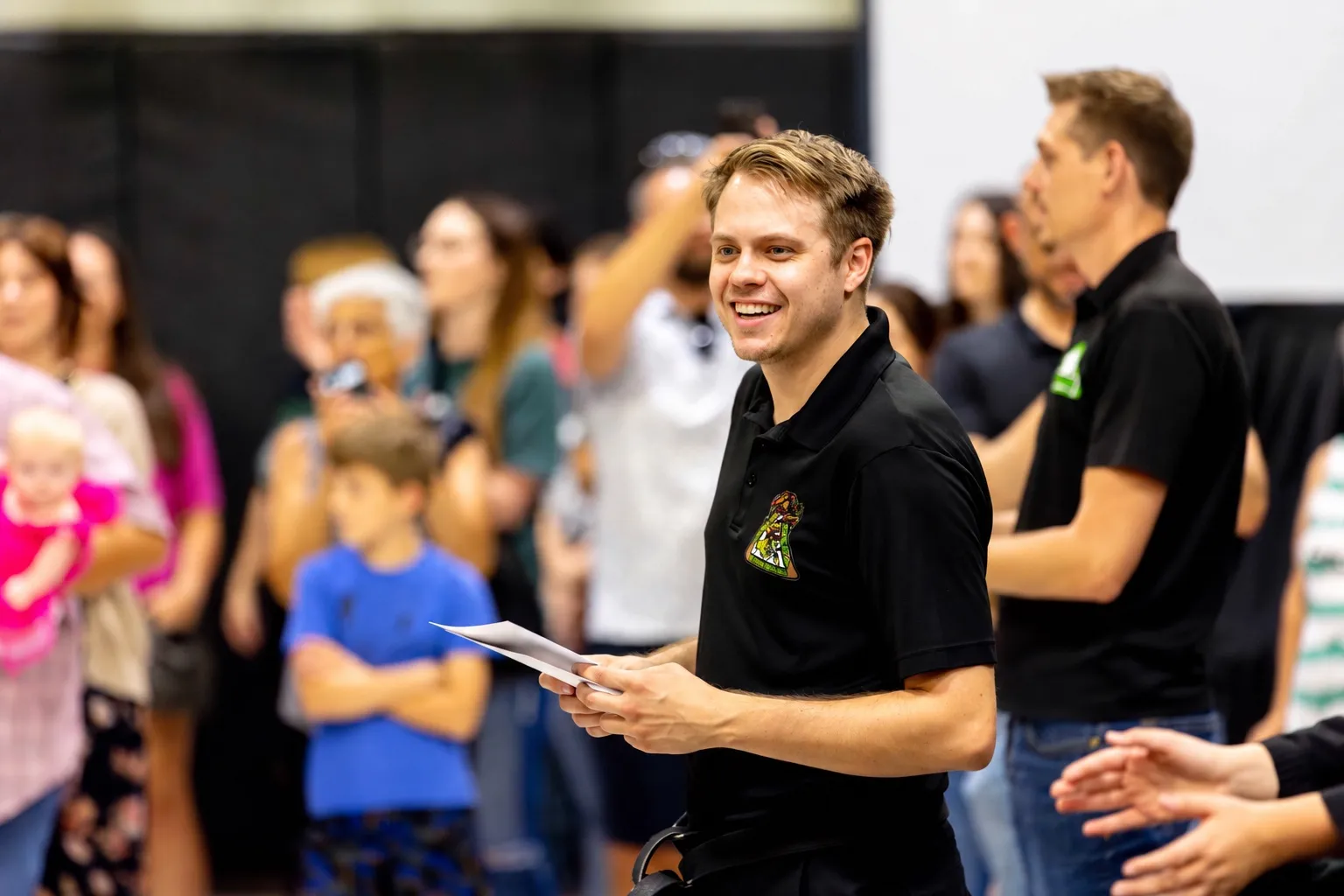 Smiling in front of a packed room at a karate school event.